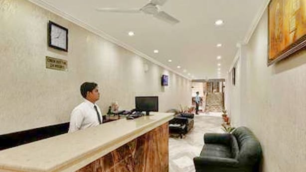 Zona de recepción de un hotel con un mostrador de mármol, un escritorio de recepción, un sofá de cuero negro y un ventilador de techo.