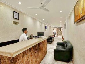 Un hall d’hôtel avec un comptoir en marbre, un bureau d’accueil, un canapé en cuir noir et un ventilateur de plafond.