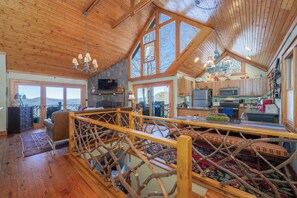 Ein großzügiger Loft-Raum mit hohen Decken, großen Fenstern, einer Holzbalkendecke und einer gemütlichen Sitzecke mit Blick ins Freie.