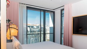 A hotel room with a large window, a bed, a lamp, and a TV. - Mama Shelter Lisboa  (Lisbon)