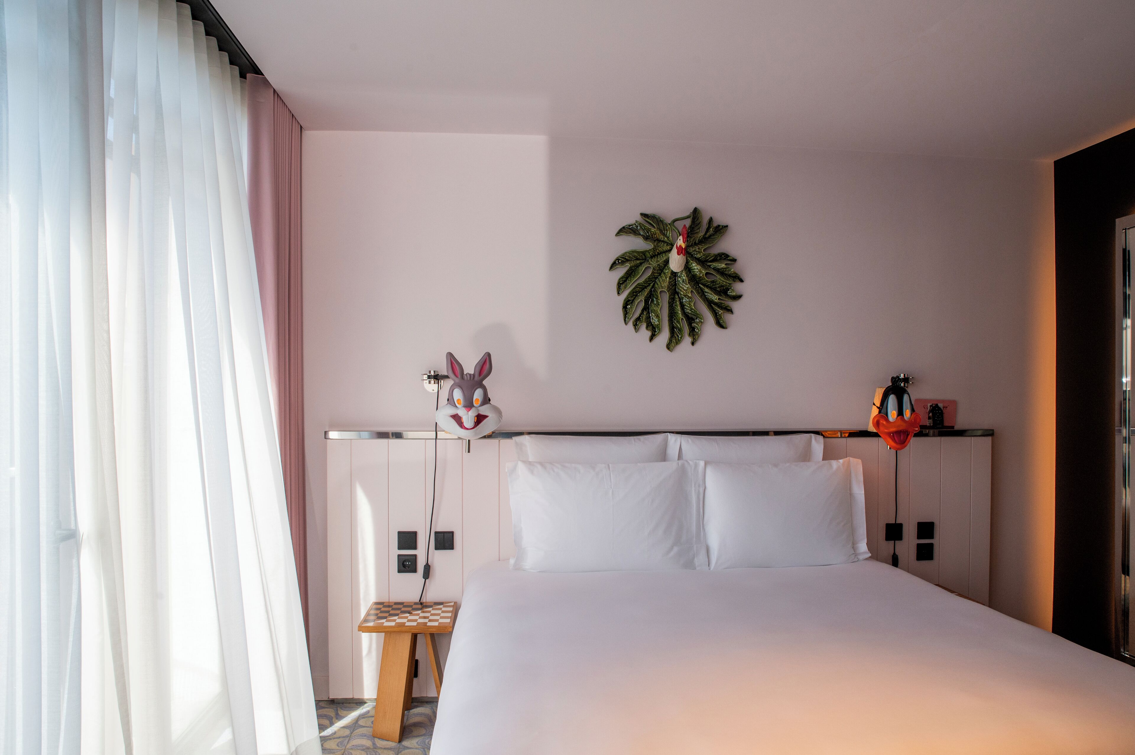 Et hotelværelse med en seng, et lille trænatbord, et vægur og en dekorativ plante.