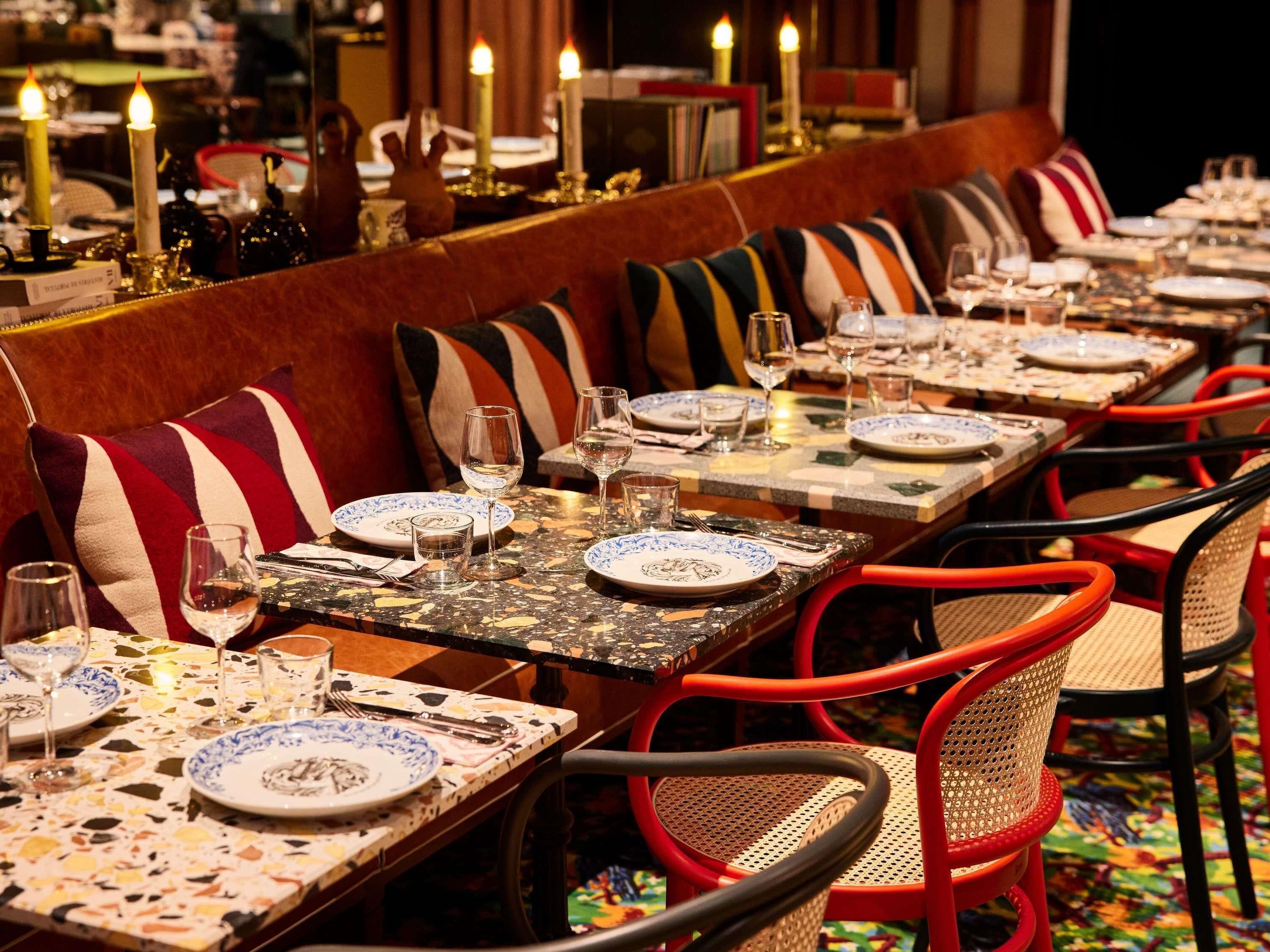 A restaurant with long communal tables, red chairs, and striped cushions.