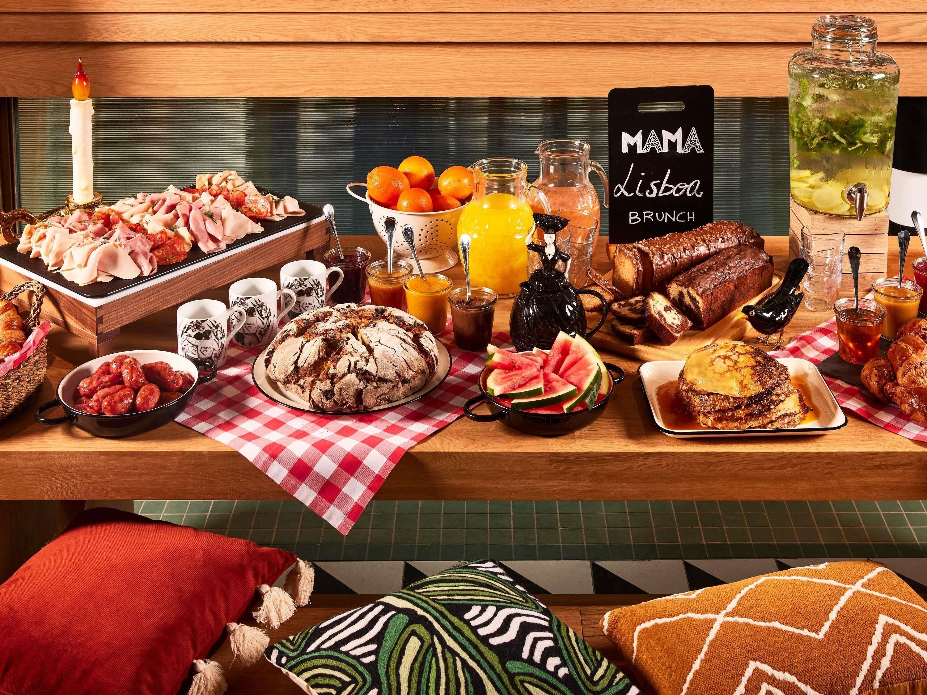 A breakfast buffet with various food items, a sign reading 'Mama Lisboa Brunch', and a candle on the table.