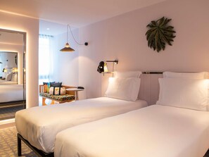 A hotel room with two beds, a small table with a chair, a wall-mounted lamp, and a decorative leaf on the wall. - Mama Shelter Lisboa  (Lisbon)