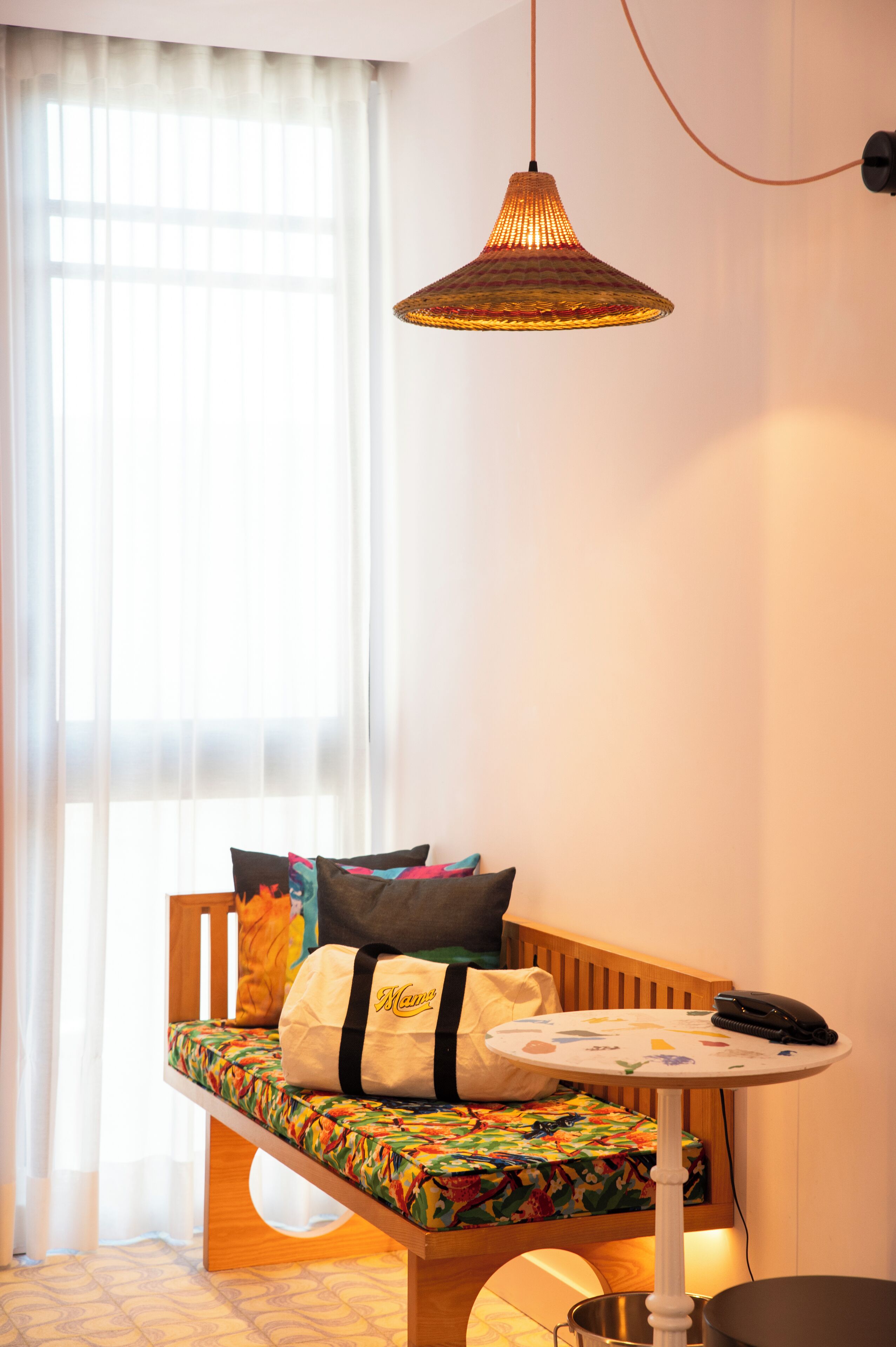 Una habitación acogedora con una cama de madera tipo banco, una mesita redonda con un teléfono y una lámpara colgante.