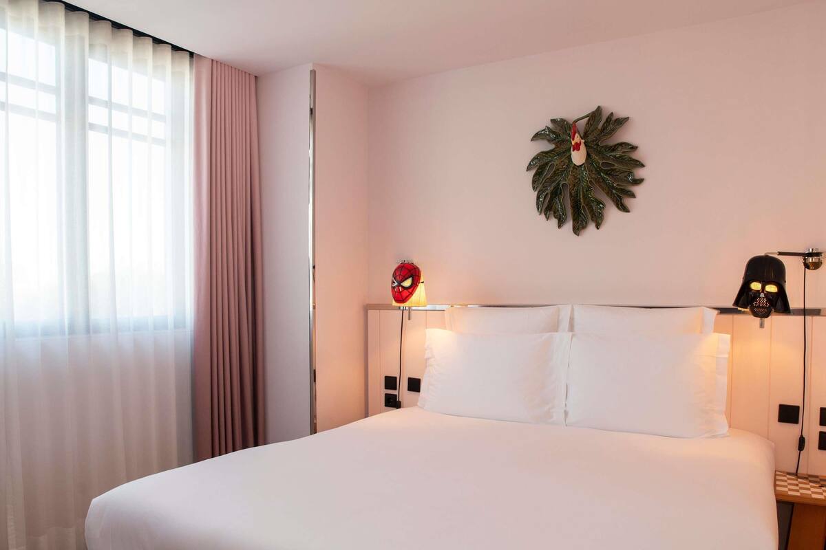 A hotel room with a large bed, a wall-mounted Spider-Man lamp, a Darth Vader lamp, and a decorative plant.