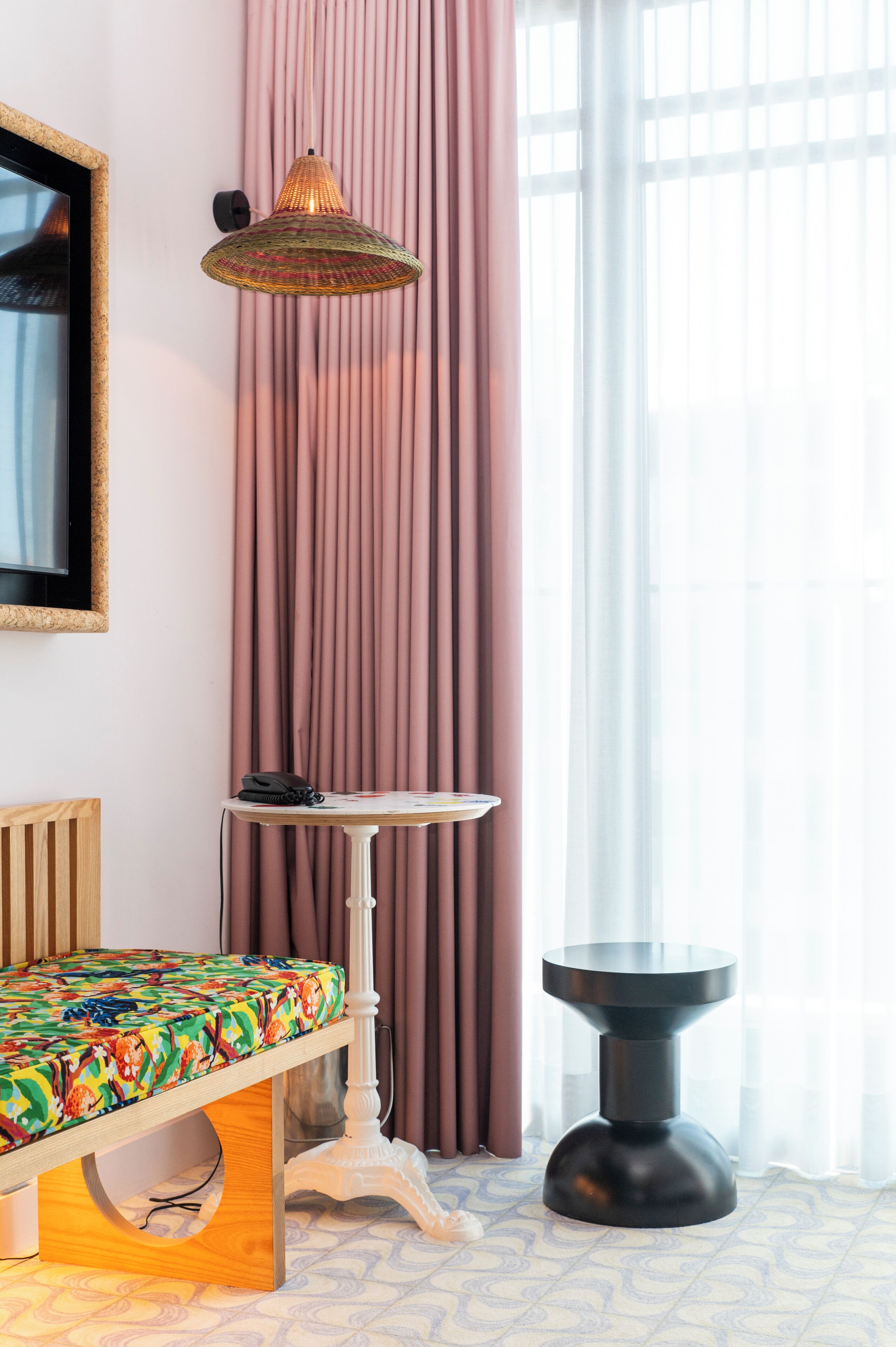 Ein Zimmer mit einem Bett, einem kleinen Tisch, einer Stehlampe und einem großen Fenster mit Vorhängen.
