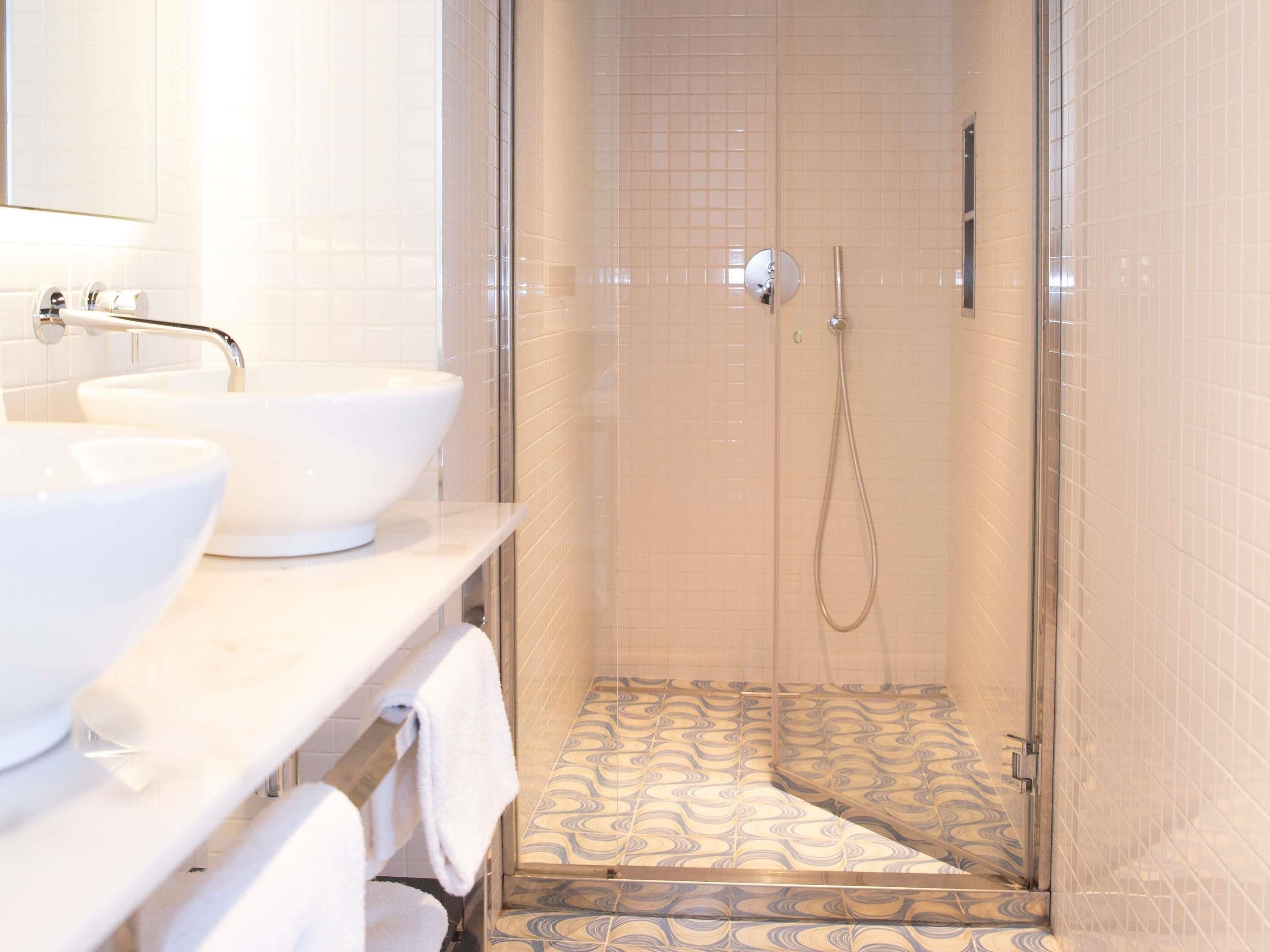 A bathroom with two white sinks, a glass shower enclosure, and patterned floor tiles.
