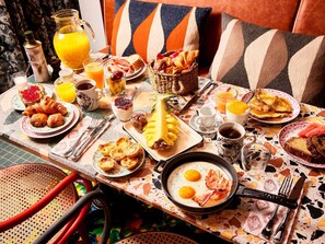 A breakfast table with various food items, a pitcher of orange juice, and a frying pan with eggs. - Mama Shelter Lisboa  (Lisbon)