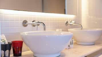 Un baño con dos lavamanos blancos, una taza de vidrio roja y una taza negra sobre el mostrador.