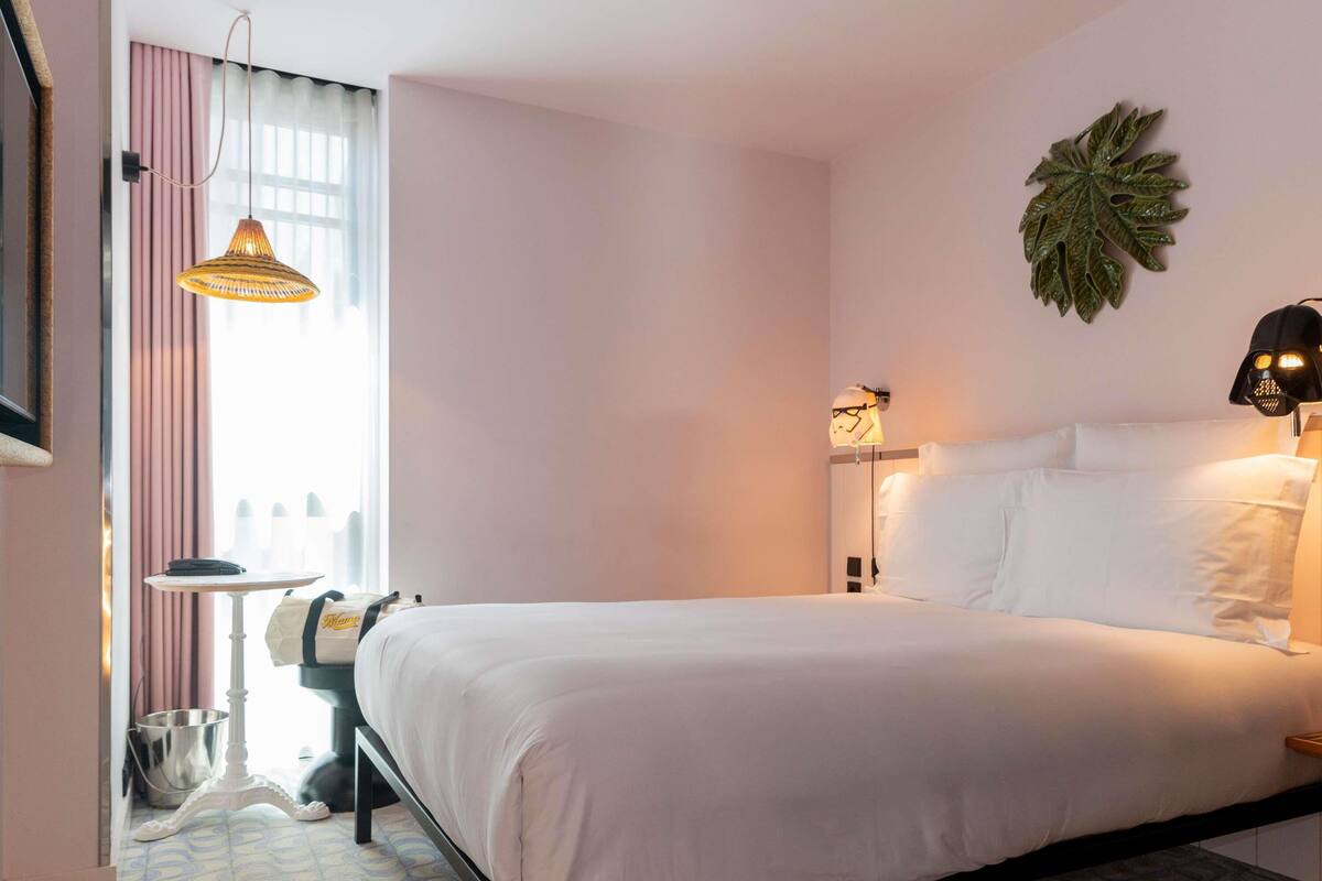 A neatly arranged hotel room with a bed, bedside lamps, a wall-mounted plant, and a window with curtains.