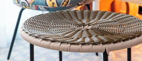 A wicker chair with a woven seat and black metal legs, a colorful patterned armchair, and a small round table with a phone on it.