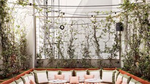 A cozy seating area with a sofa and round tables, surrounded by greenery and a large window. - Mama Shelter Lisboa  (Lisbon)