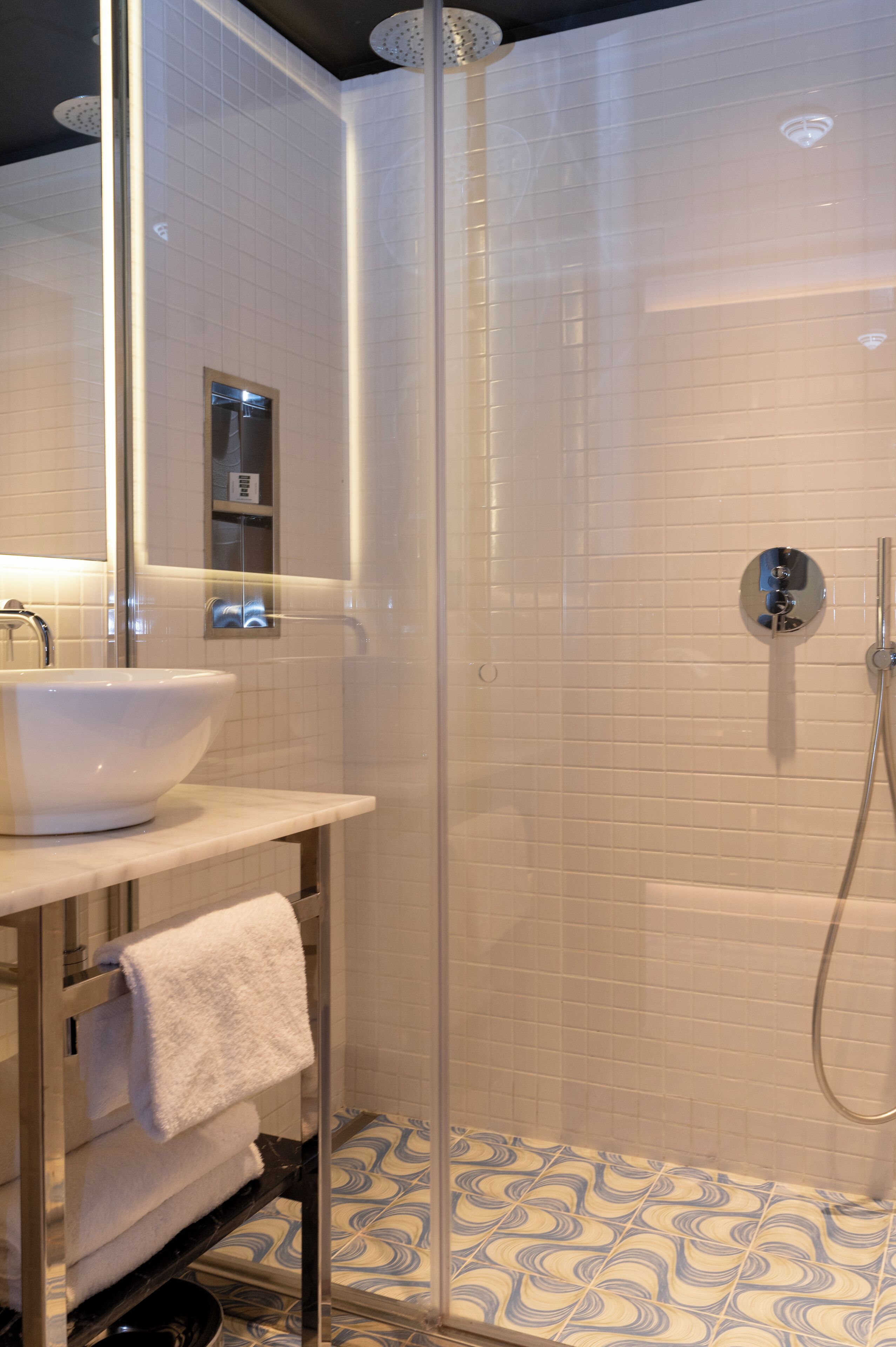 Een moderne badkamer met een douchecabine van glas, een witte wastafel en een vloer met een patroon.