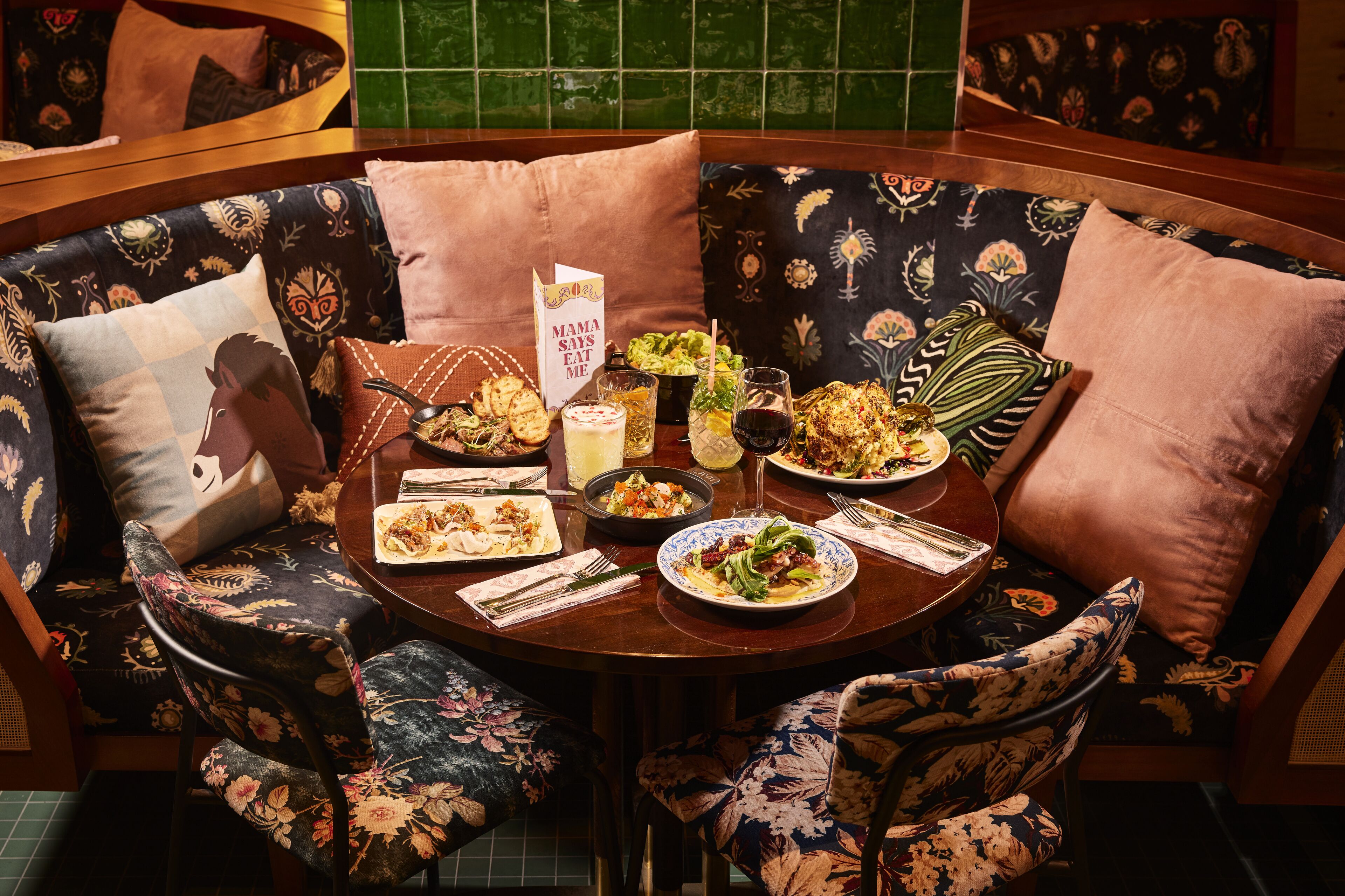 A round dining table with floral upholstery and a variety of dishes, including salads and a dessert, set for a meal.