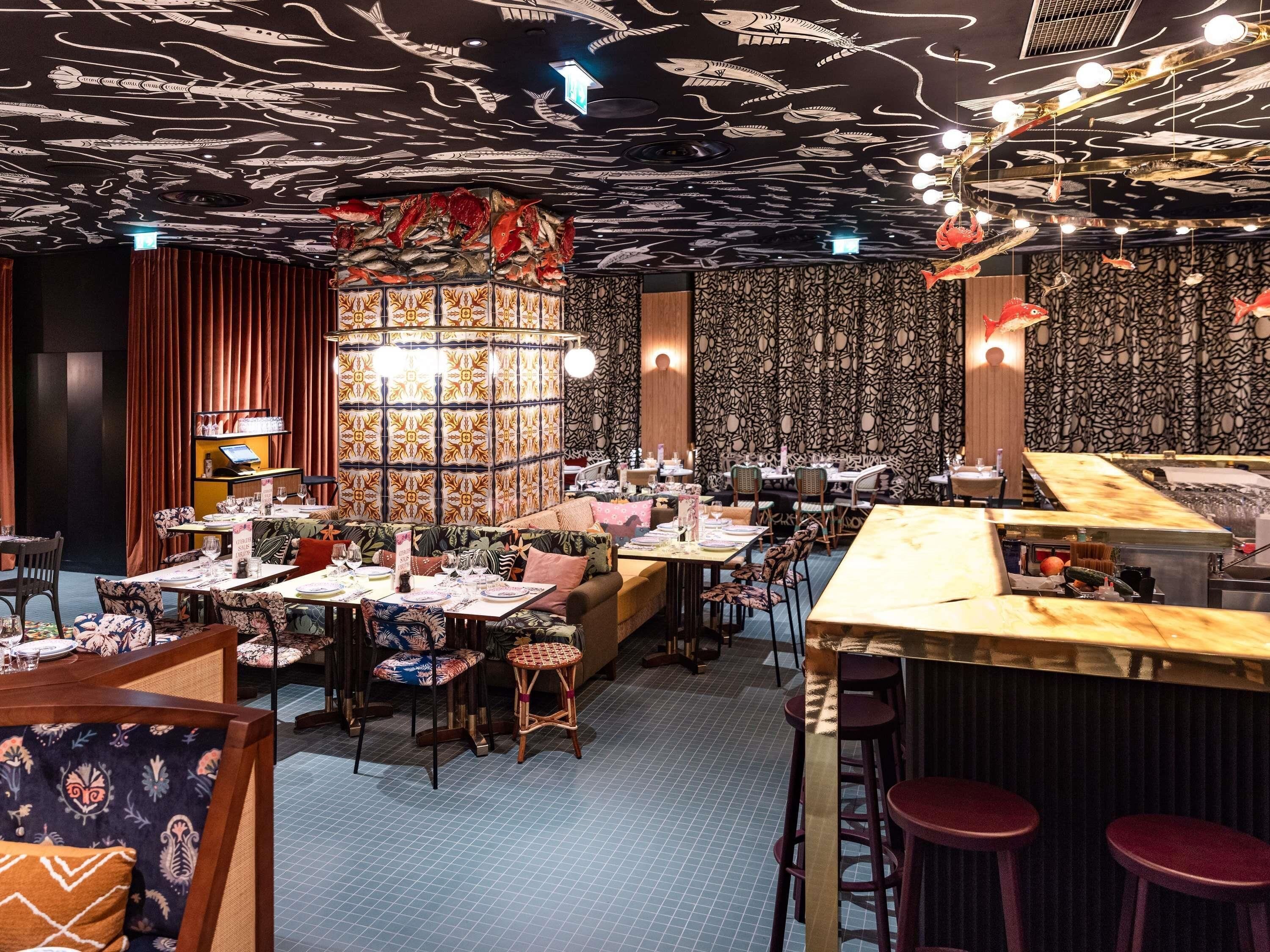 A restaurant with a ceiling decorated with fish patterns, tables with chairs, and a bar area.