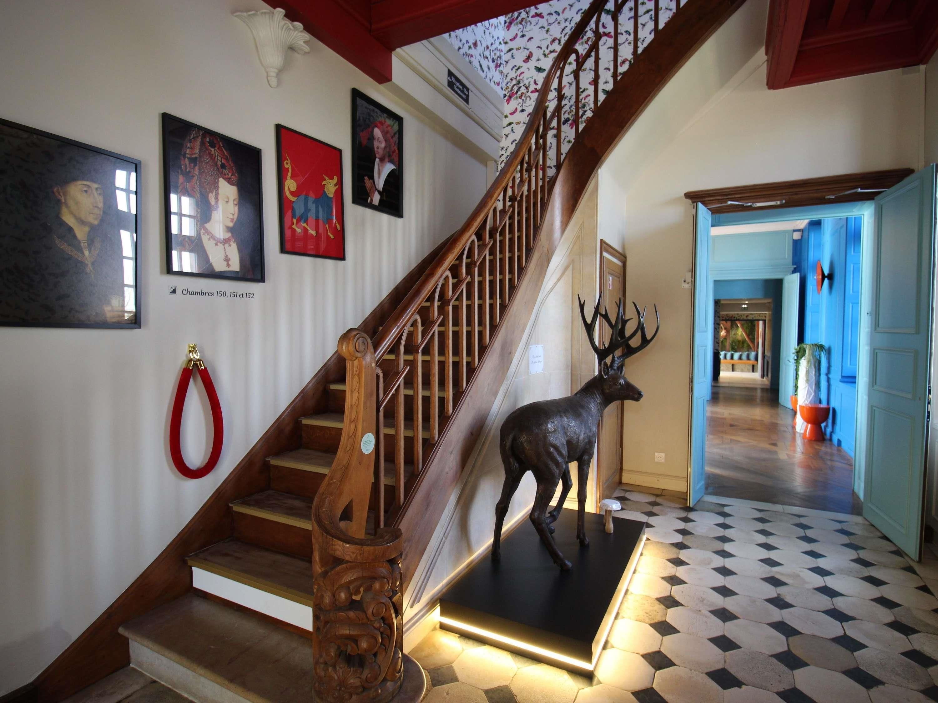 Un escalier avec une rampe en bois, une laisse rouge et une statue de cerf sur un socle noir.