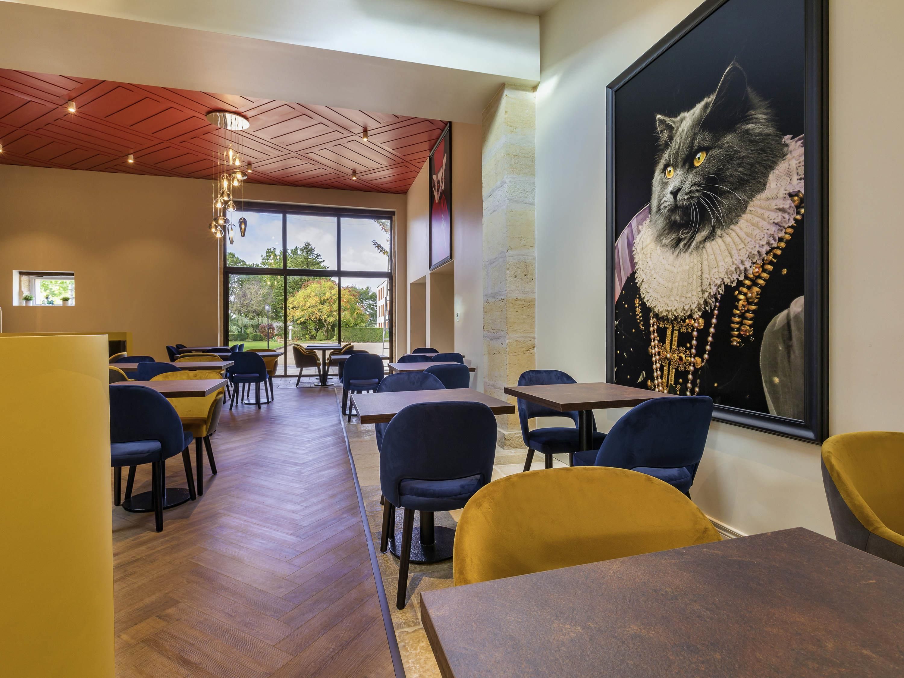 Ein Restaurant mit Holzböden, blauen und gelben Stühlen und einem großen Katzenbild in einem Rahmen an der Wand.