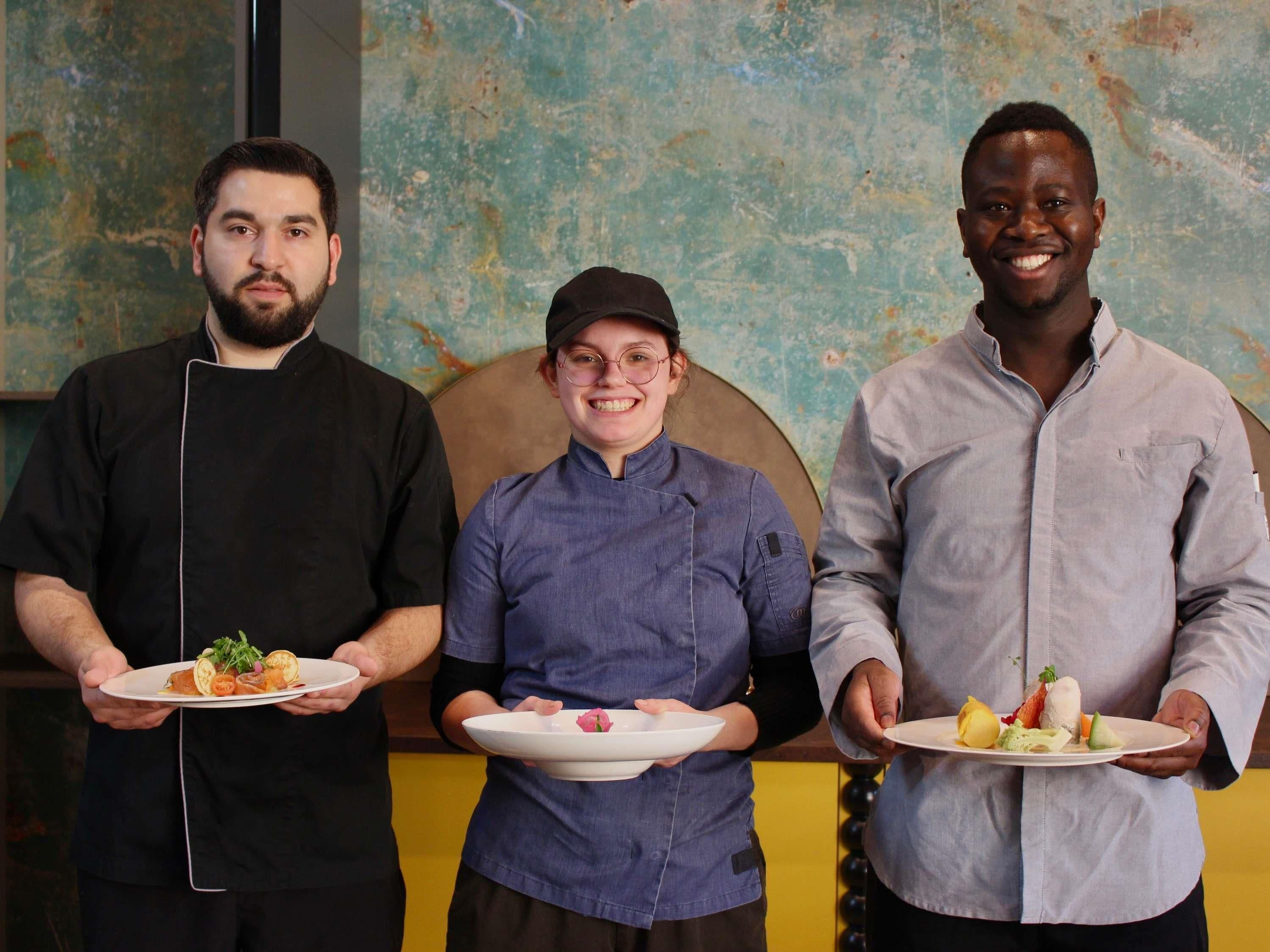 Three individuals holding plates of food in a room with a textured wall.