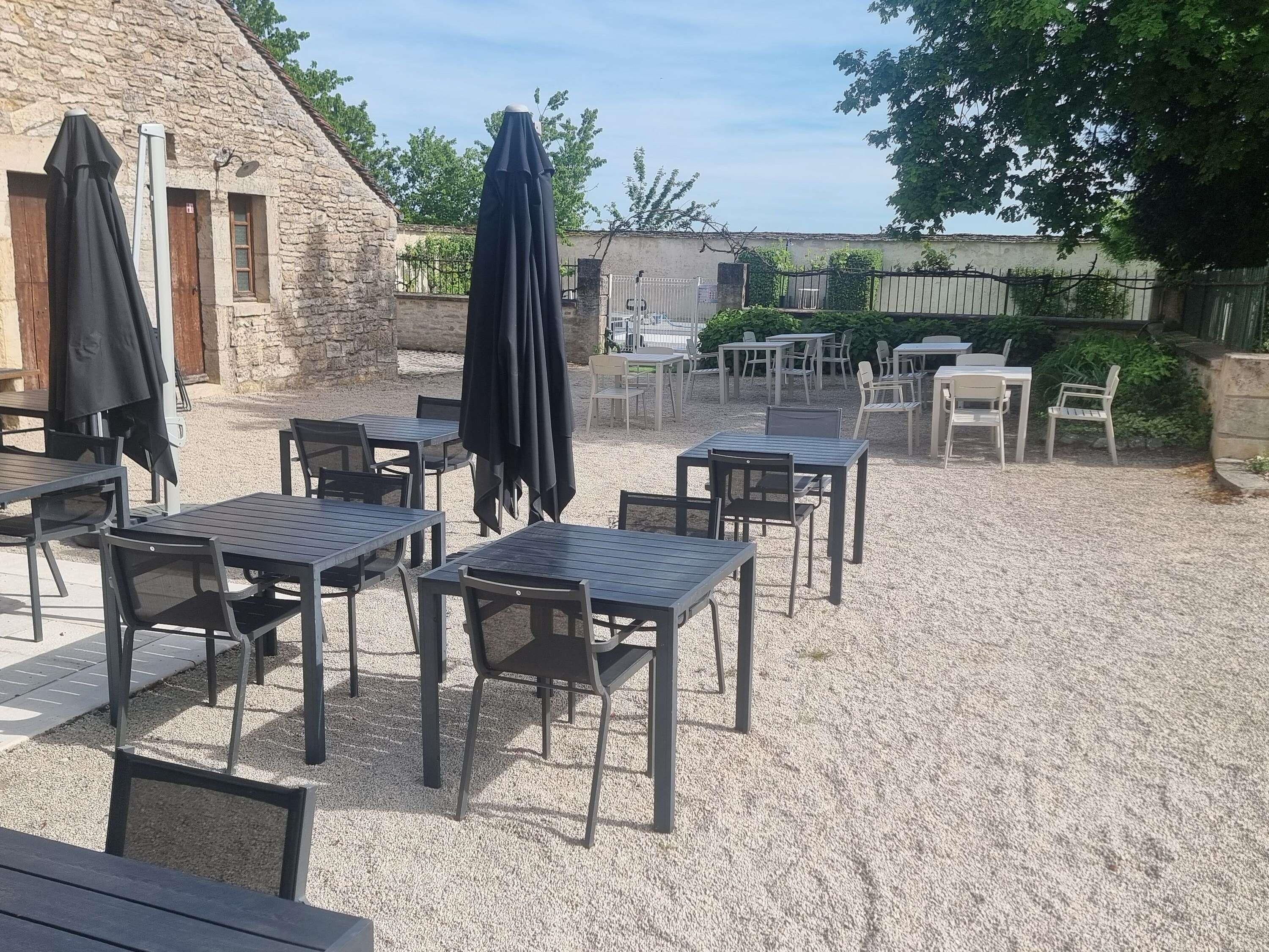 Un patio al aire libre con mesas y sillas, un edificio de piedra y una cerca.