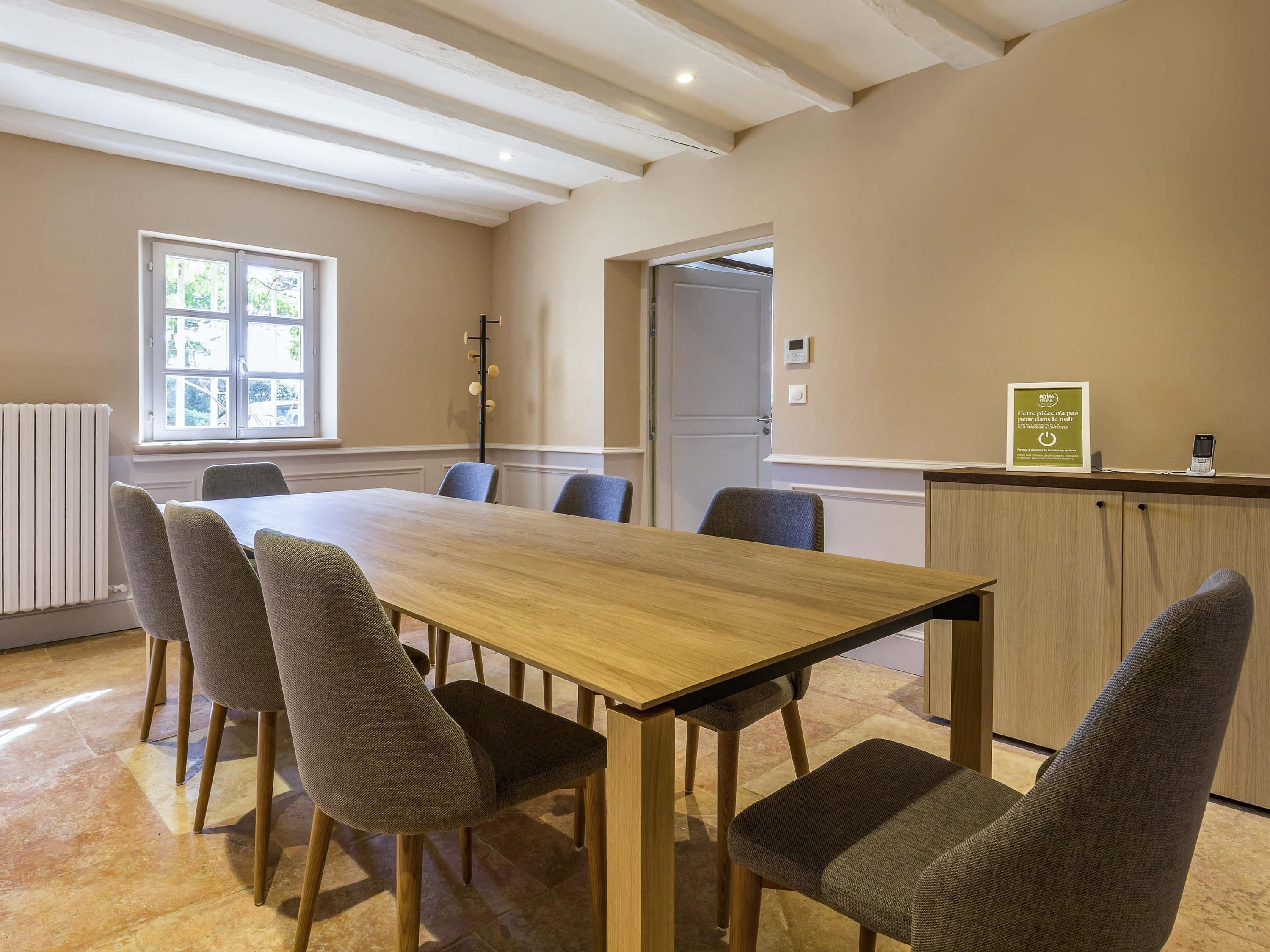 A conference room with a long table, six chairs, a radiator, a window, and a door.