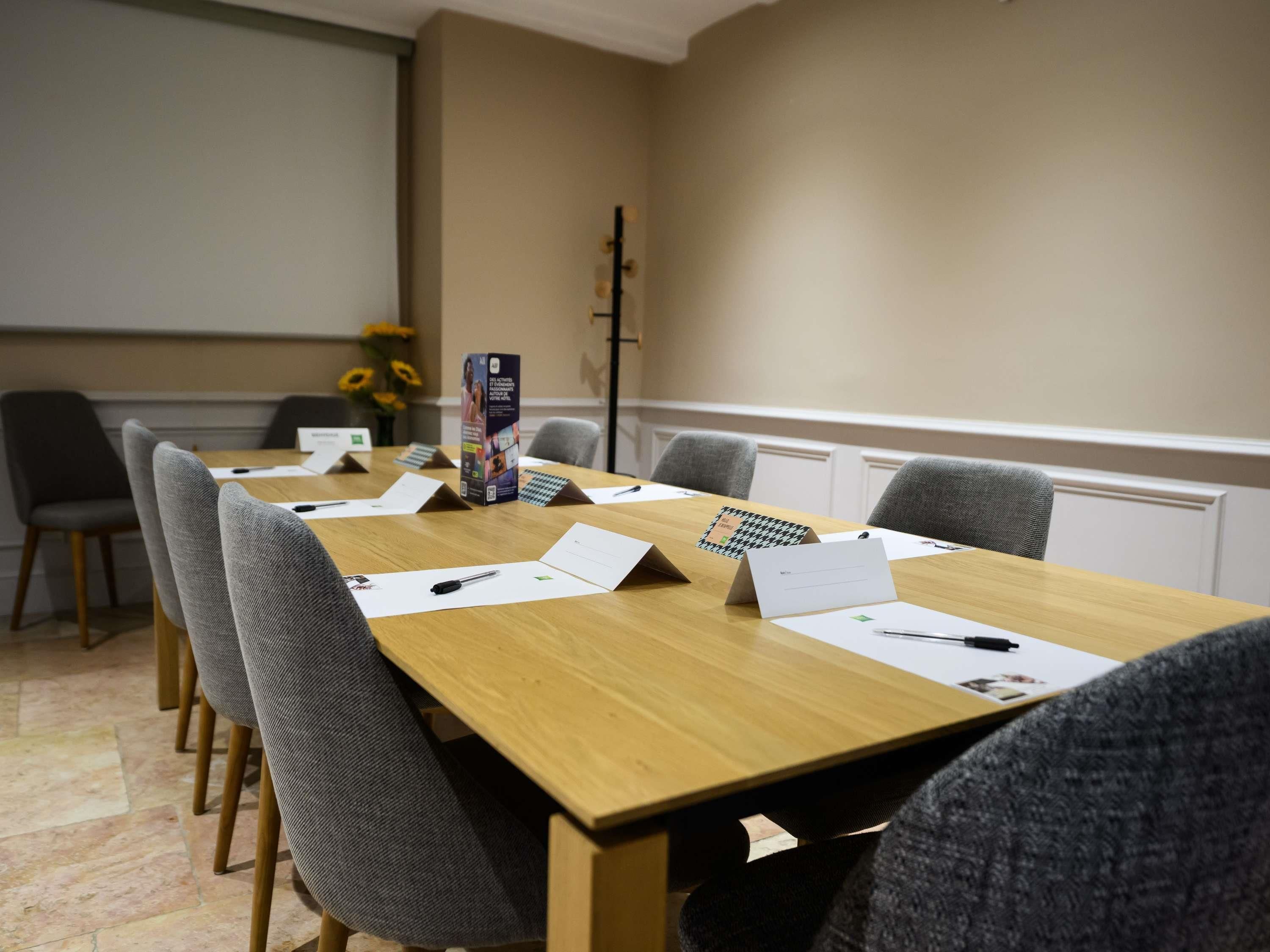 A conference room with a long table, chairs, nameplates, and a projector screen.