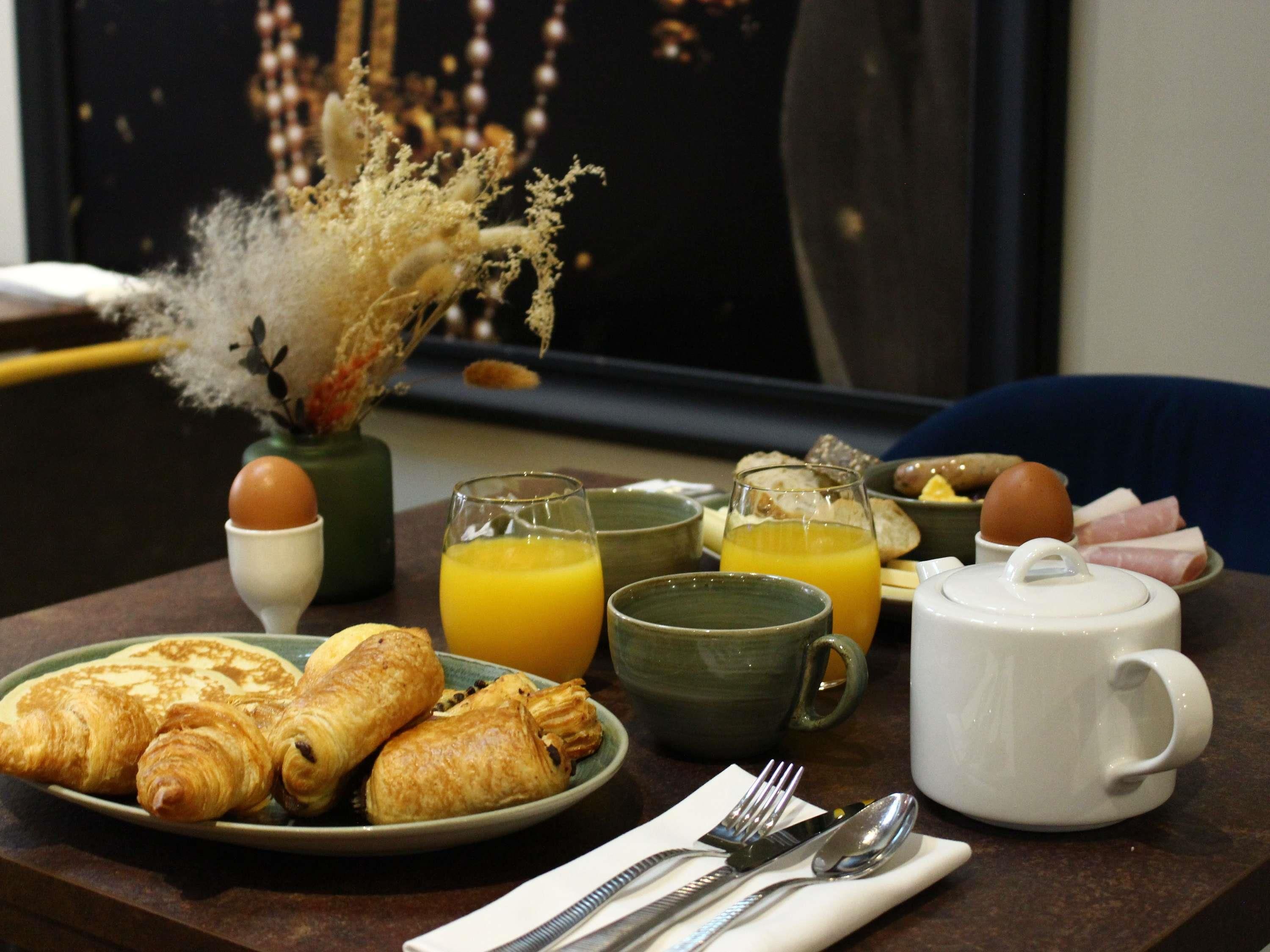 A breakfast table with croissants, eggs, orange juice, and a teapot.