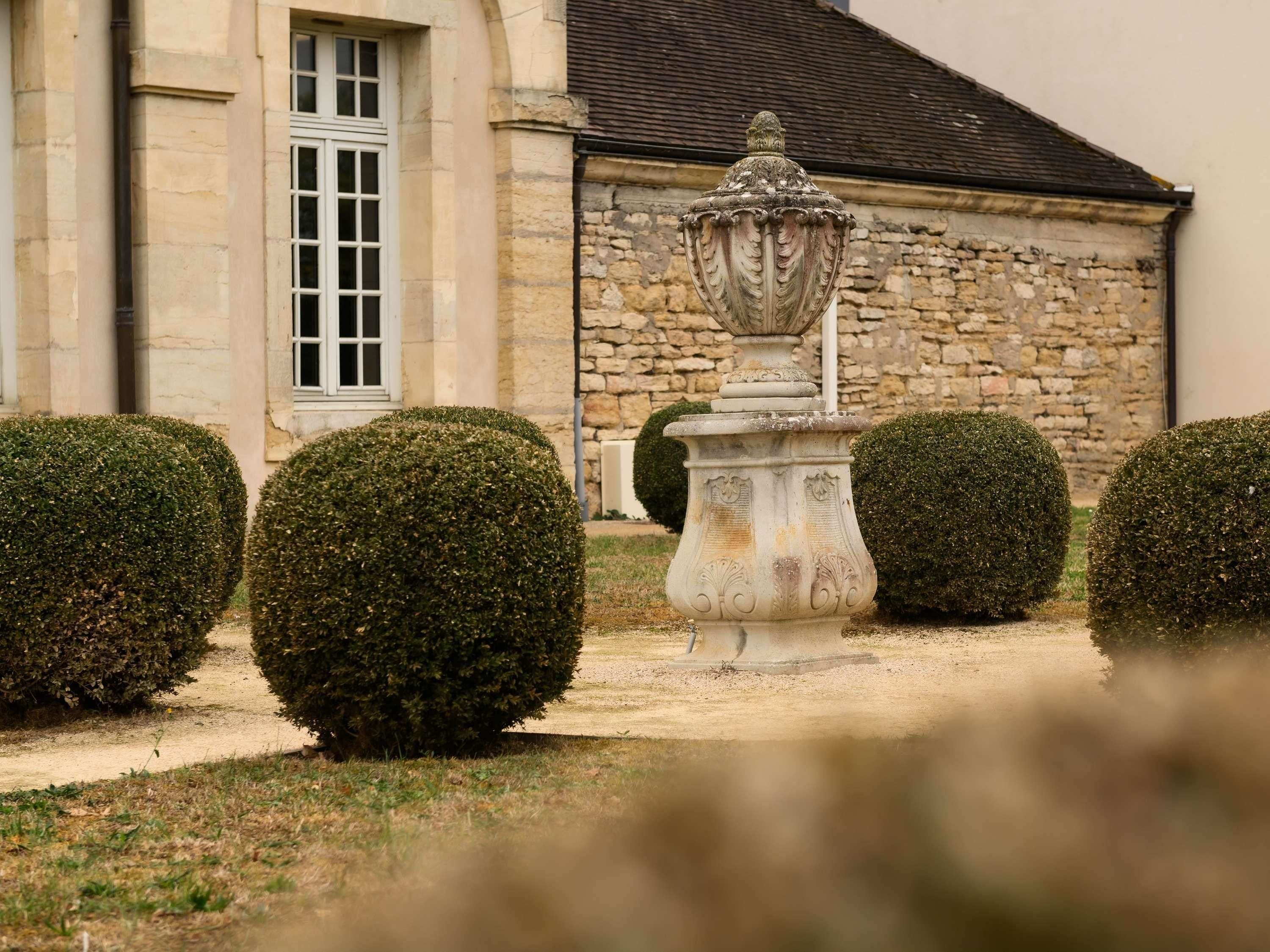 Un bâtiment en pierre doté d’une fenêtre et orné d’une urne décorative dans le jardin.