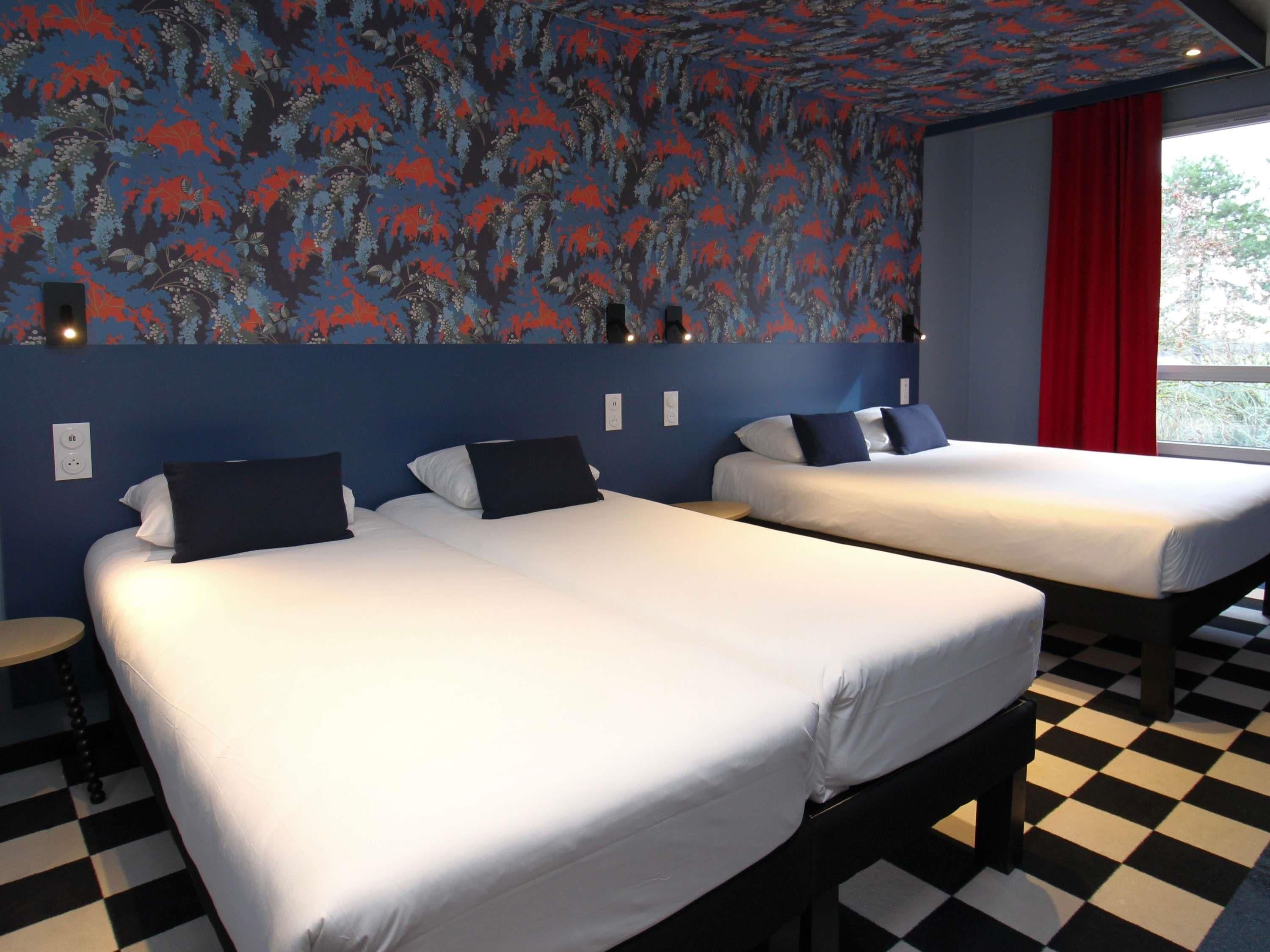 Une chambre d’hôtel avec deux lits, un sol à carreaux et un mur orné d’un motif floral.