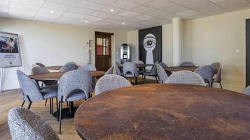 A conference room with round tables and grey upholstered chairs, a projector screen, and a wall-mounted clock.