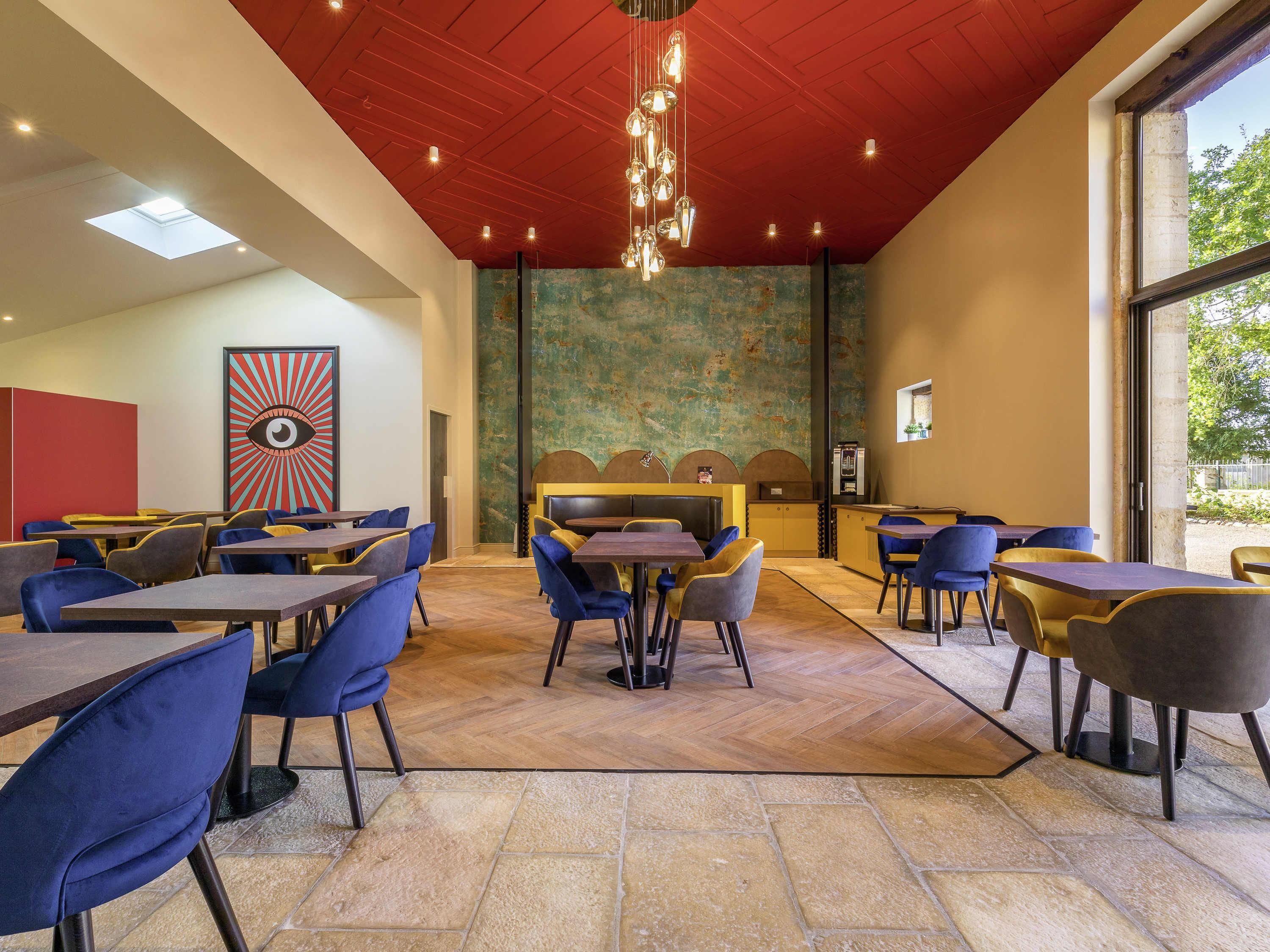 A restaurant with a red ceiling, blue and yellow chairs, and a large window.