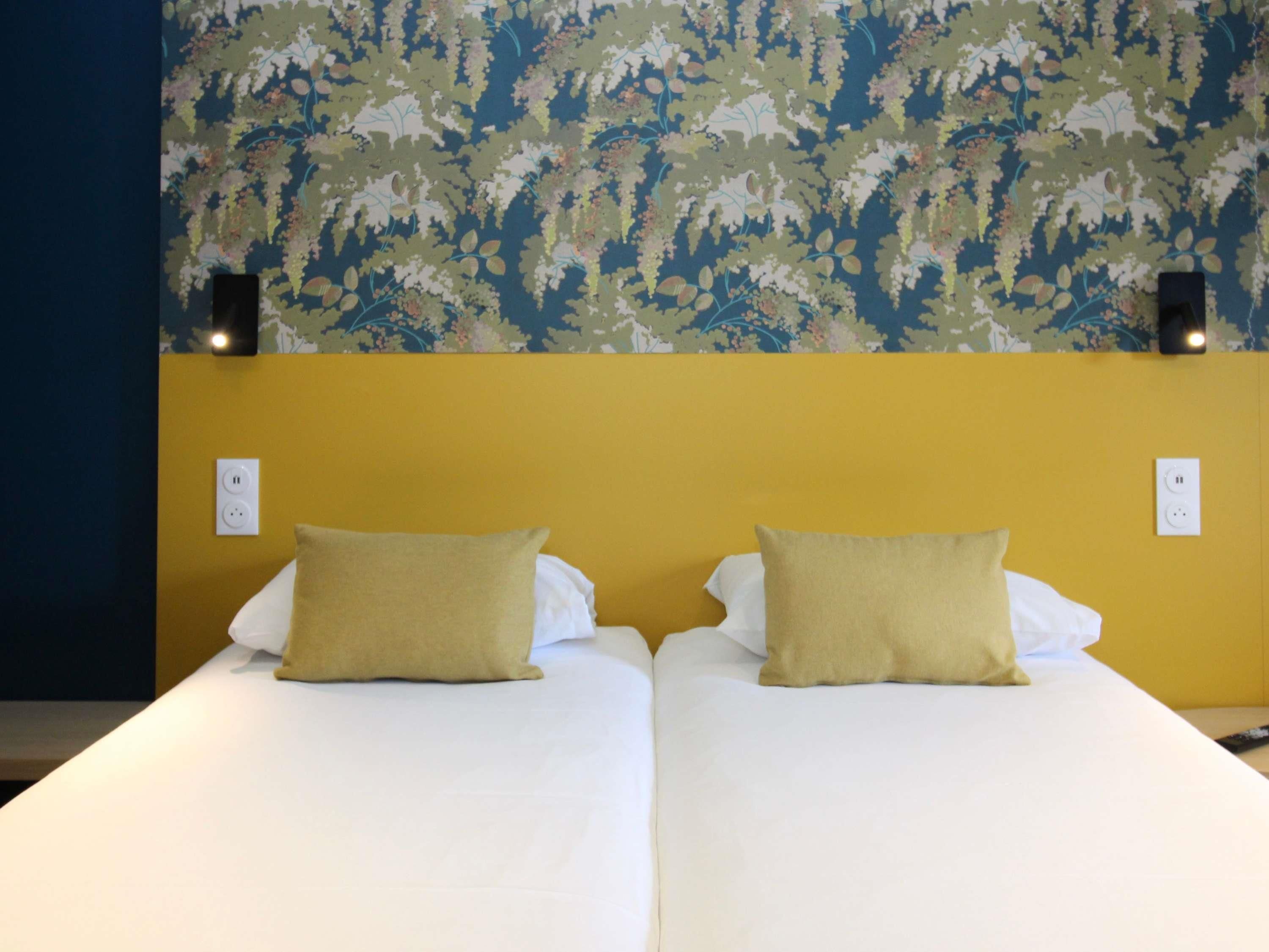 A double bed with two pillows, a yellow wall, and a floral wallpaper.