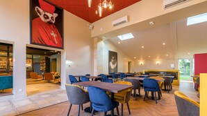 A spacious dining area with multiple tables and chairs, a large wall mural, and a view of the outdoors.