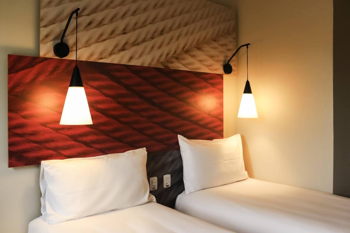 Una habitación de hotel con dos camas, un cabecero estampado en rojo y lámparas colgantes.