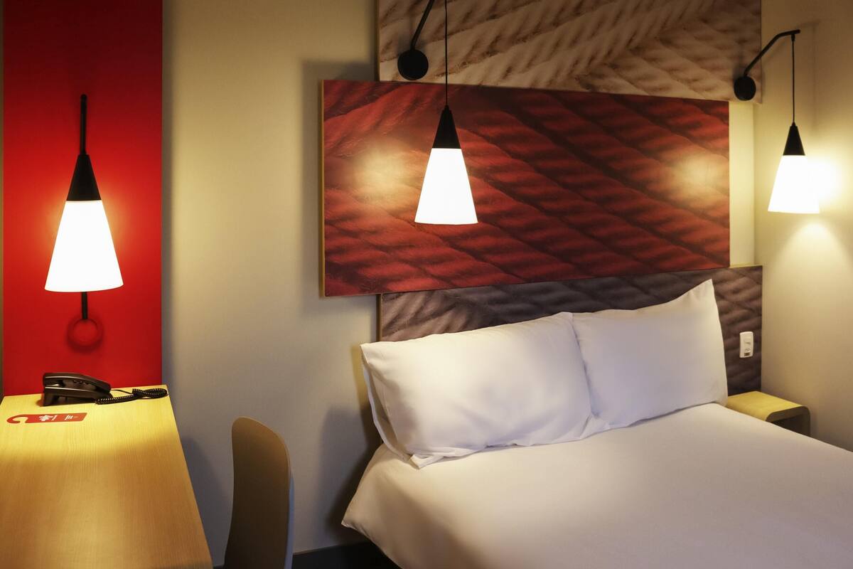 Una habitación de hotel con una cama, un escritorio con teléfono y dos lámparas colgantes.