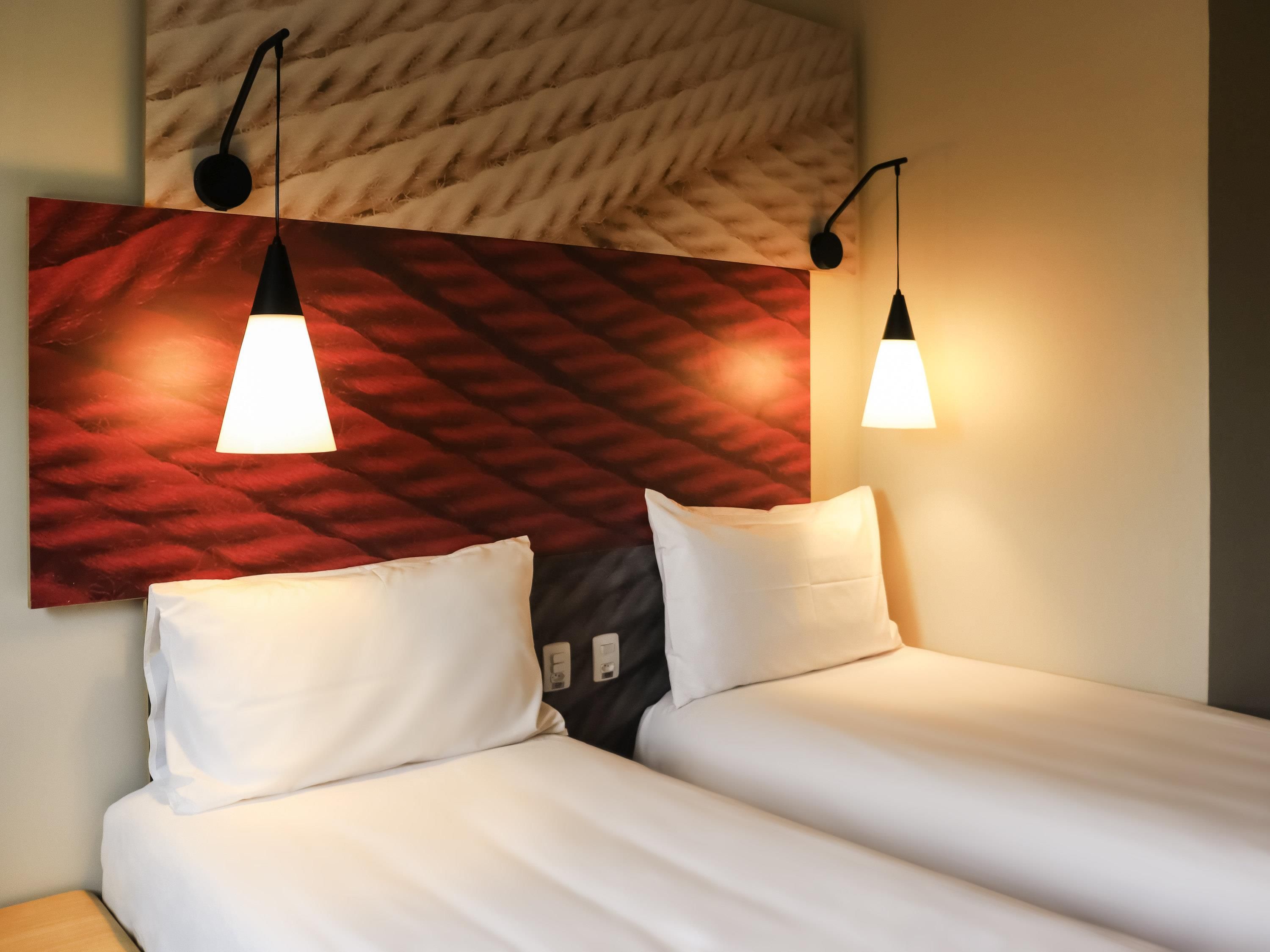 A hotel room with two beds, a red patterned headboard, and pendant lights.