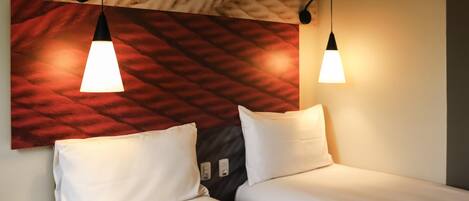 A hotel room with two beds, a red patterned headboard, and pendant lights.