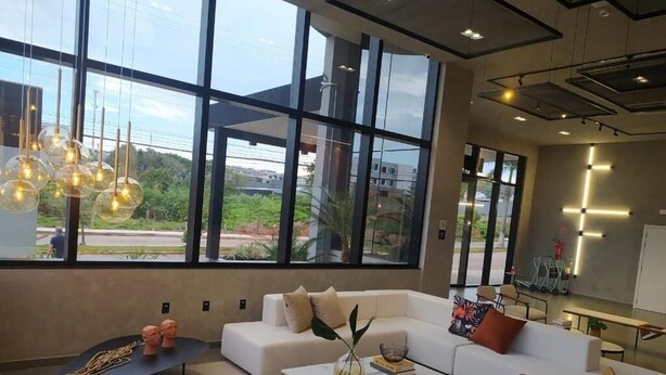 A modern living room with large windows, a sectional sofa, a coffee table, and a wooden chair. -  Serrana Residence Hotel  (Nova Serrana)