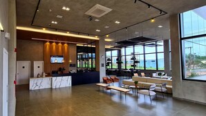 A modern reception area with a marble counter, seating area, and large windows offering a view. -  Serrana Residence Hotel  (Nova Serrana)