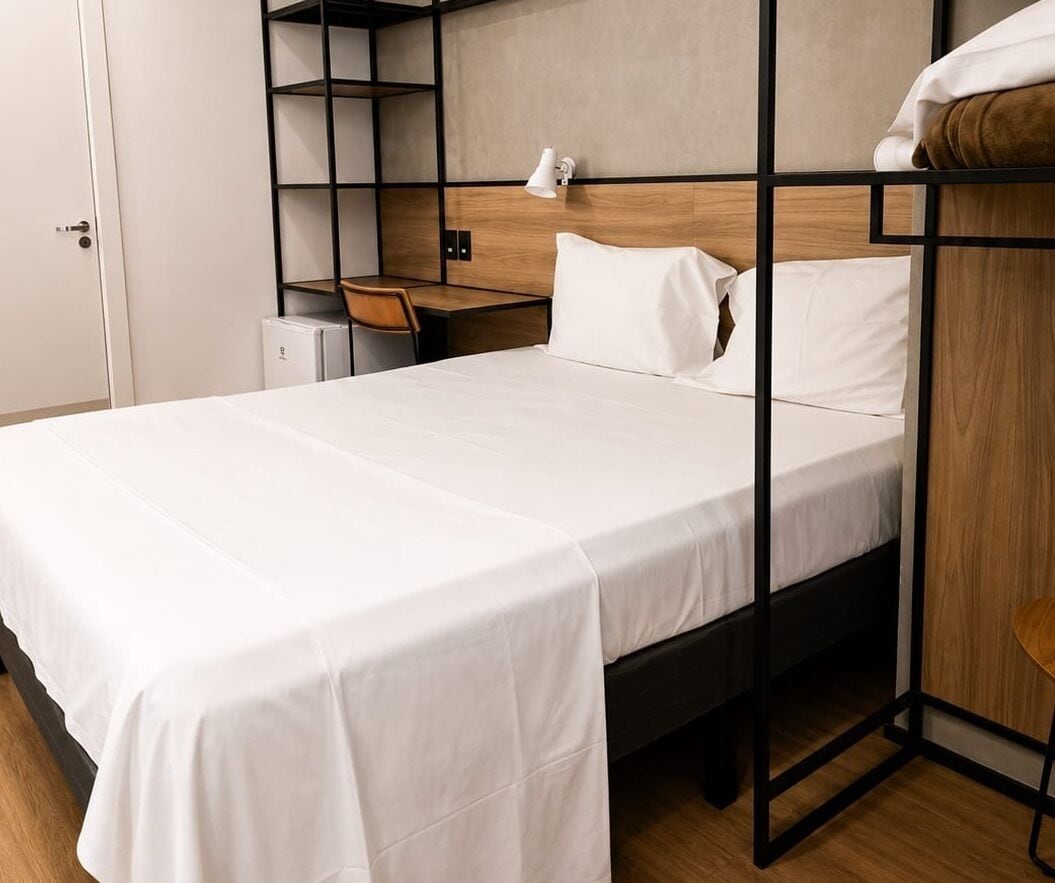 Una cama litera con colchón blanco, cabecero de madera y un escritorio con silla.