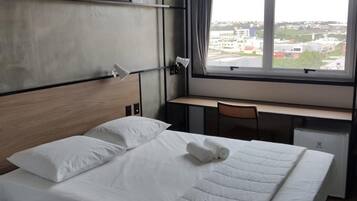 A hotel room with a bed, a desk, a chair, a window with a view, and artwork on the wall.
