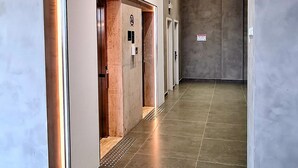 A modern hallway with a metallic elevator, recessed lighting, and a tiled floor. -  Serrana Residence Hotel  (Nova Serrana)