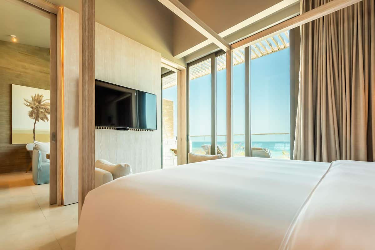 A hotel room with a large bed, a TV mounted on the wall, and a view of the sea.