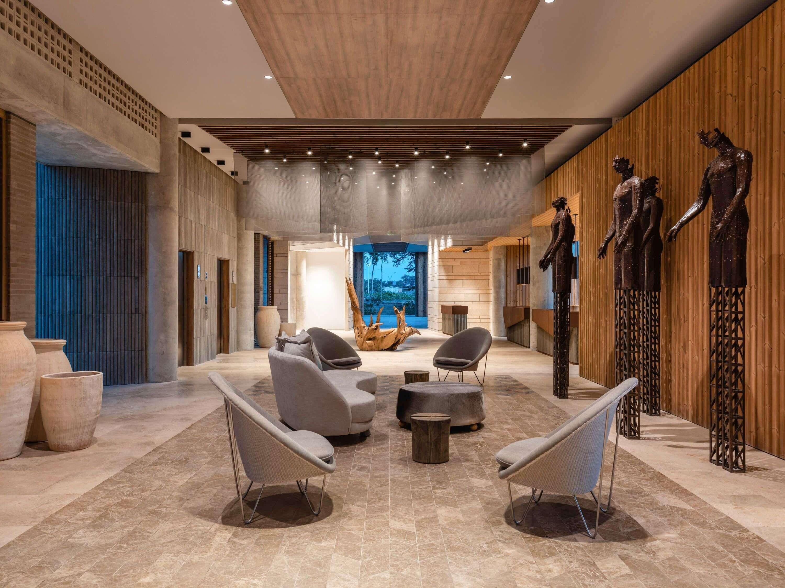 Un vestíbulo amplio con asientos modernos, una gran escultura de madera y vistas al exterior.