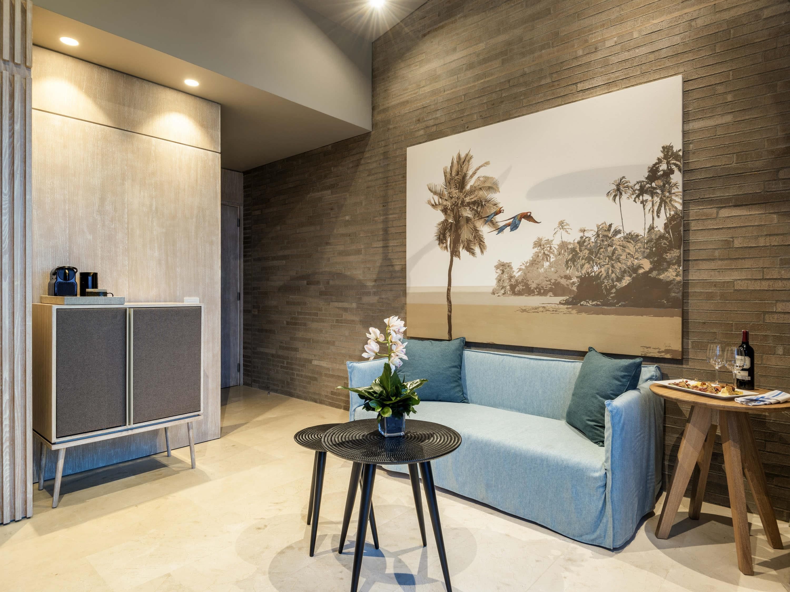 A modern living room with a sofa, a small round table with a vase of flowers, a cabinet, and a wall-mounted artwork depicting a beach scene.