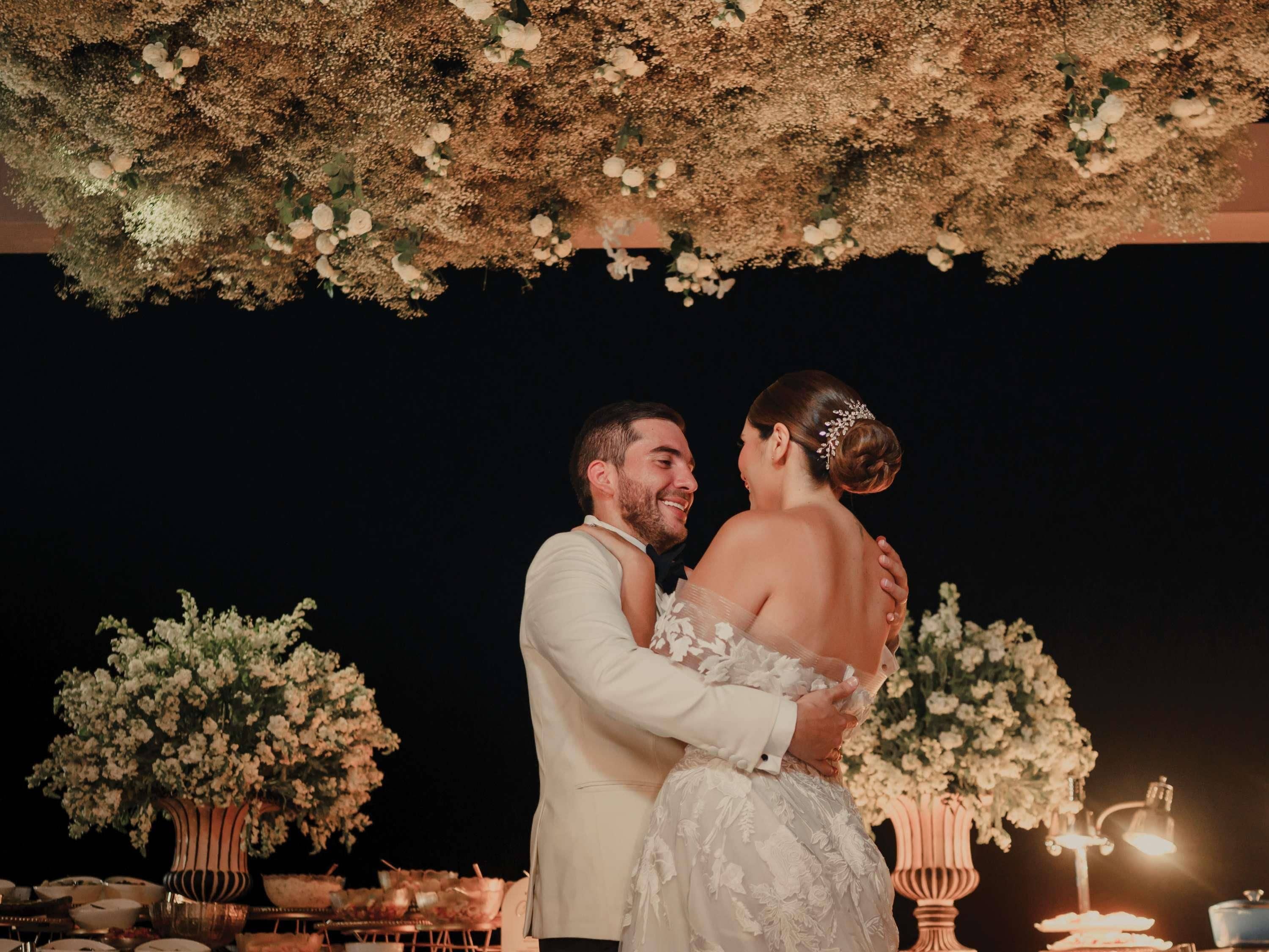 Um casal se abraçando sob um dossel de flores em uma recepção de casamento.
