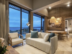 A modern living room with a sofa, chairs, a dining table, and large windows offering a view.