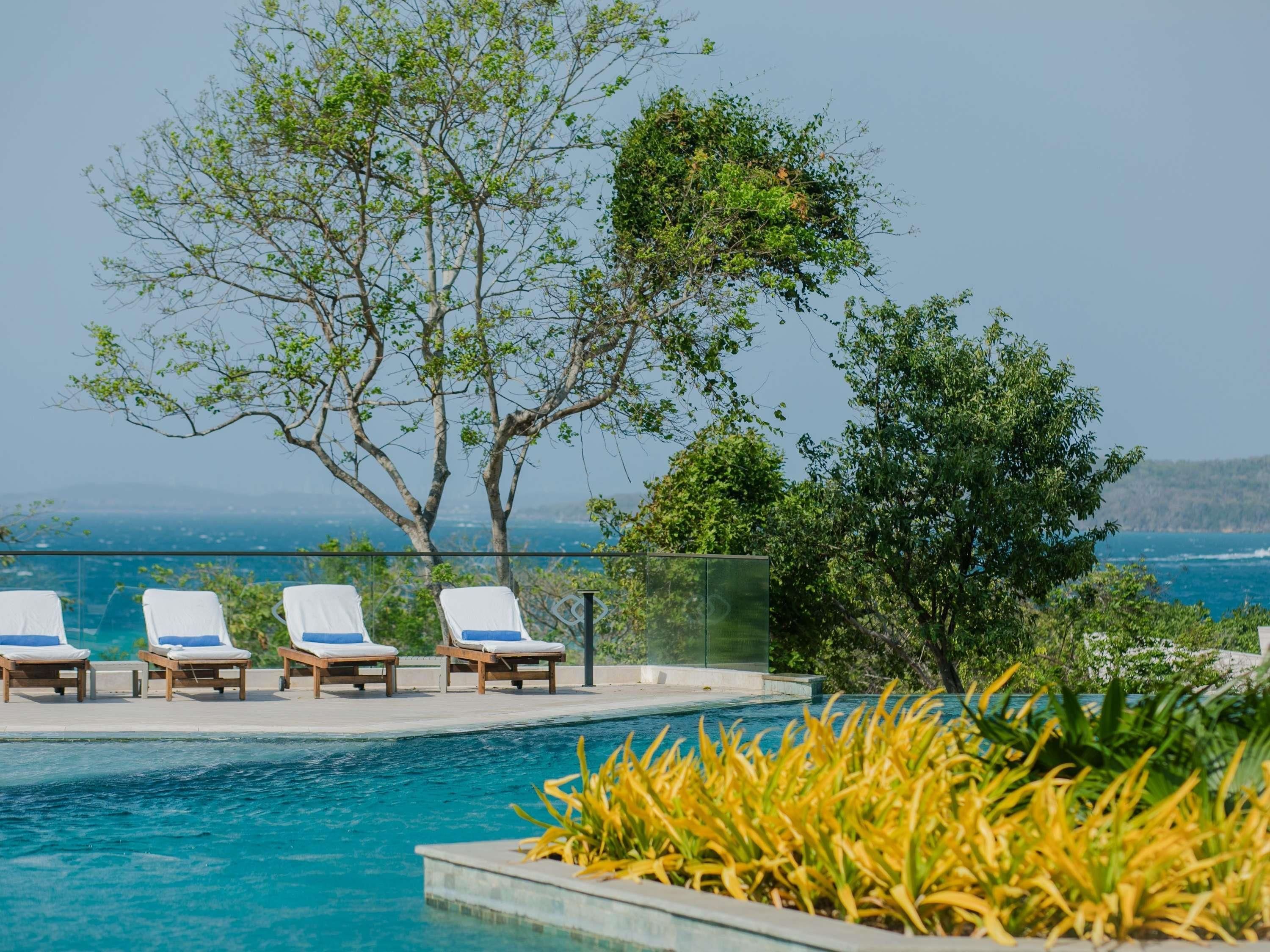 Un área junto a la piscina con sillones de descanso y vista al océano.