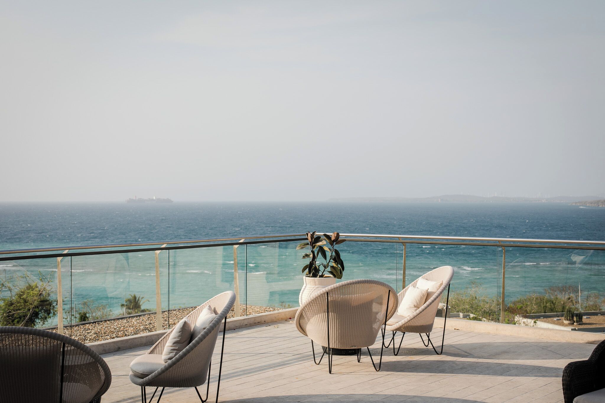 Une terrasse avec des fauteuils en osier donnant sur une vue panoramique de la côte.