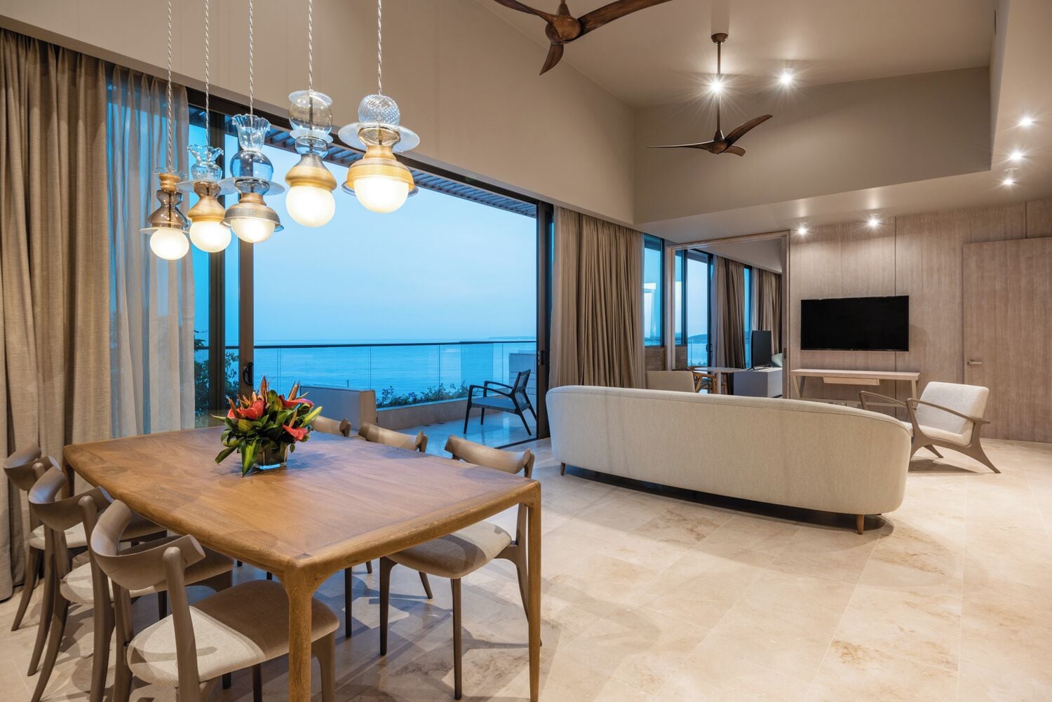 A modern living room with a dining area, large windows with a view, and a flat-screen TV.